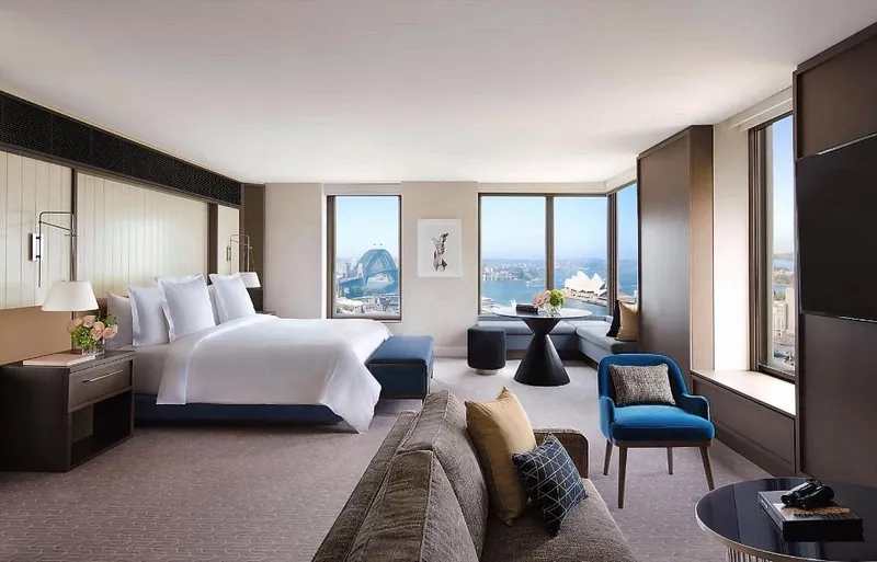 Four Seasons Hotel Sydneyの客室のベッドと窓際の席、窓外の港の風景